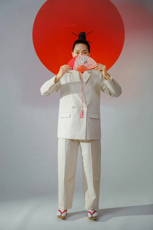 a woman holding a fan in front of her face, an album cover, inspired by Koson Ohara, unsplash, neo-dada, subject detail: wearing a suit, wearing off - white style, full body portrait shot, photographed for reuters