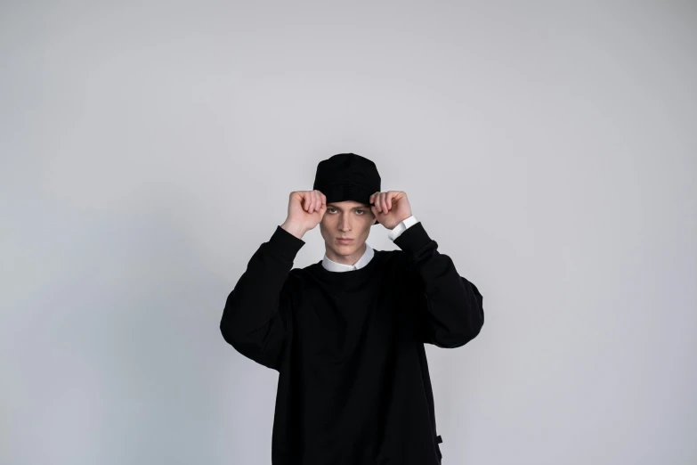 a man standing in front of a white wall, a character portrait, by Attila Meszlenyi, unsplash, black beanie, black sweater, yung lean, priest