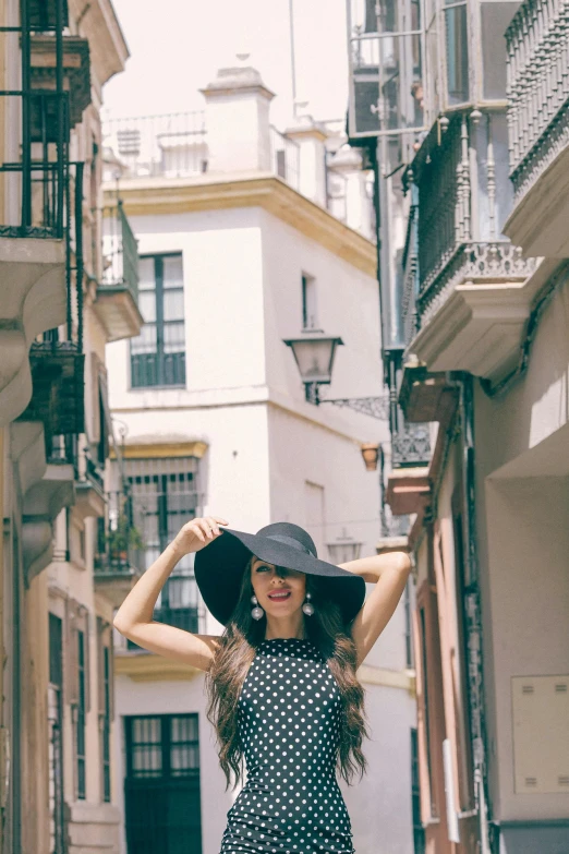 a woman in a polka dot dress and black hat, inspired by Gina Pellón, pexels contest winner, ancient city streets behind her, happy fashion model, spanish, gif