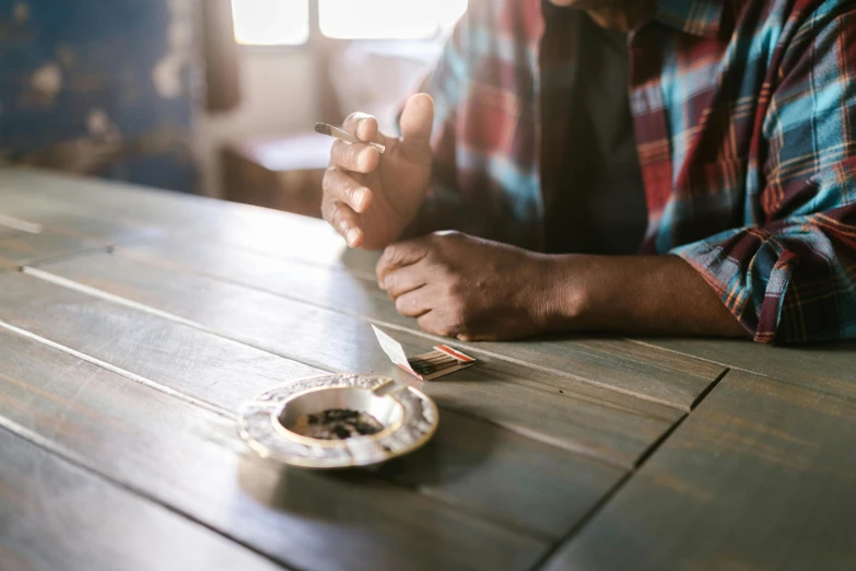 a man sitting at a table eating food, by Everett Warner, trending on pexels, praying with tobacco, beans, black man, with an ashtray on top