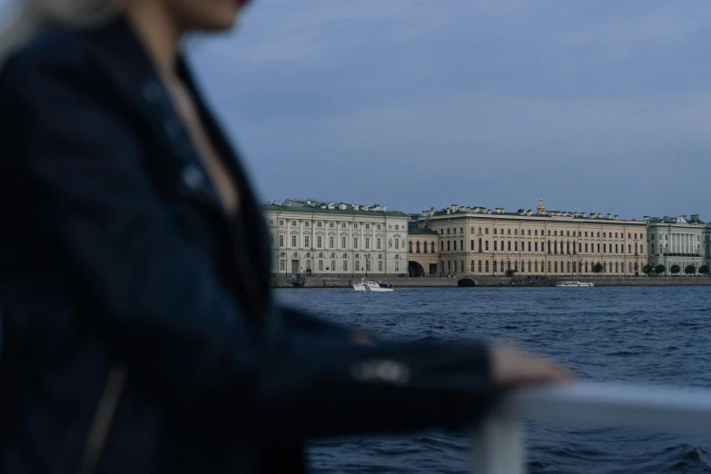 a woman standing on top of a boat next to a body of water, a picture, by Julia Pishtar, pexels contest winner, neoclassicism, photo of putin, royal palace, lit from the side, out-of-focus background