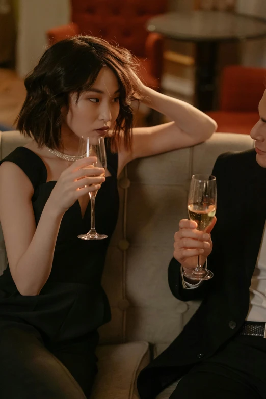 a man and a woman sitting on a couch holding wine glasses, janice sung, champagne on the table, struggling, asian women