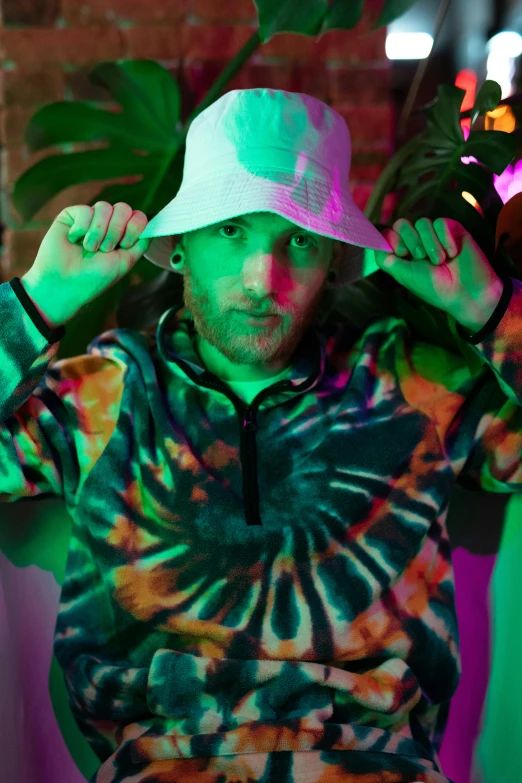 a man sitting in a chair with a hat on, an album cover, inspired by Kyle Lambert, unsplash, renaissance, tie-dye, flashing lights, pewdiepie, man in adidas tracksuit