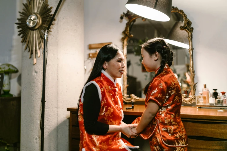 a couple of women standing next to each other in front of a mirror, pexels contest winner, cloisonnism, wearing red attire, reaching out to each other, young asian girl, vintage inspired