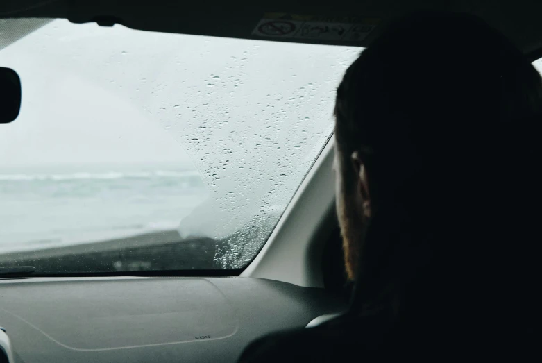 a woman driving a car in the rain, by Hallsteinn Sigurðsson, pexels contest winner, man sitting facing away, looking out at the ocean, depressed mood, view from inside