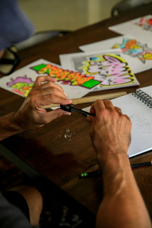 a person sitting at a table drawing on a piece of paper, by John Backderf, process art, graffiti art style, coloring book page, a high angle shot, vibrant cartoon art