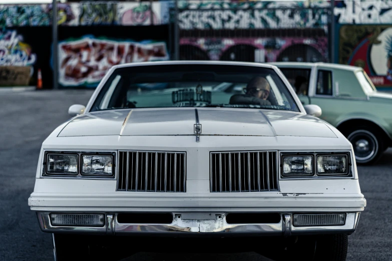 a white car parked in front of a graffiti covered building, a portrait, by Dan Frazier, pexels contest winner, lowriders, clean detail 4k, 1983, front lit