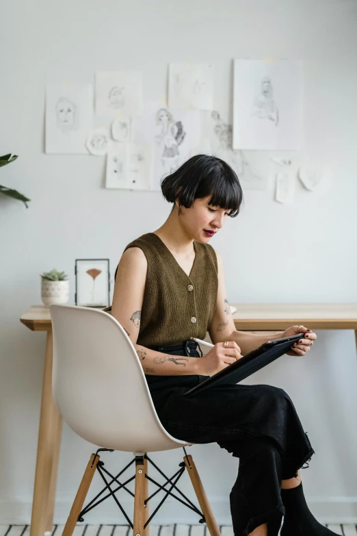 a woman sitting at a desk using a tablet computer, a drawing, inspired by Ruth Jên, pexels contest winner, sitting on designer chair, with a bob cut, architect studio, bao pham