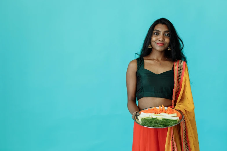 a woman holding a plate of food in front of a blue background, trending on unsplash, hurufiyya, dressed in a sari, wearing a crop top, set against a white background, promotional image