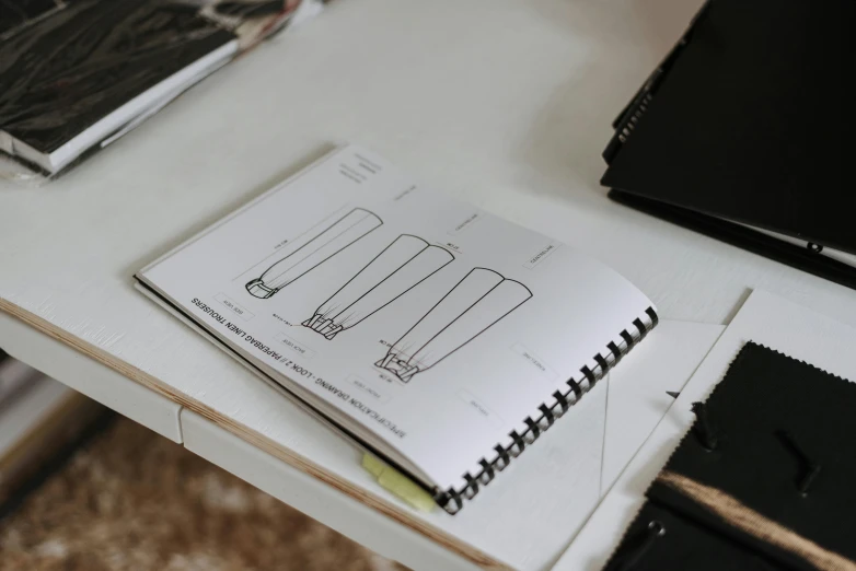 a book sitting on top of a desk next to a laptop, a wireframe diagram, by Nina Hamnett, flasks, lamps, black on white paper, casually dressed