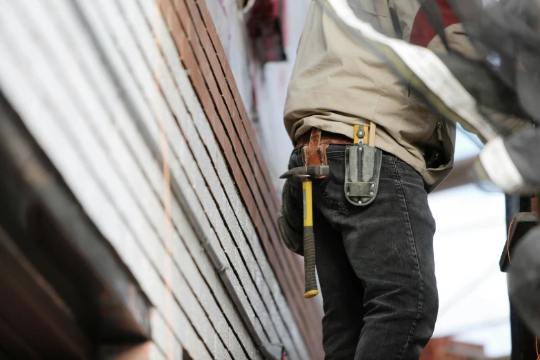 a construction worker standing on the side of a building, pexels contest winner, tool belt, hand holding a knife, grey, casually dressed