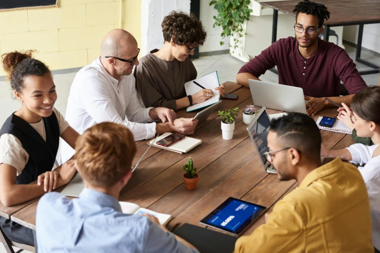 a group of people sitting around a wooden table, sitting at a computer