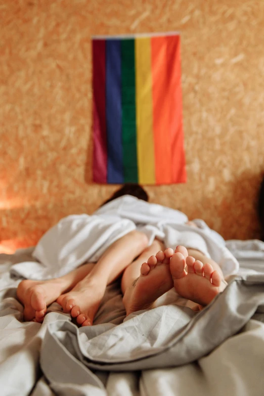 a person laying on top of a bed under a blanket, trending on pexels, renaissance, lgbt flag, two people, legs intertwined, a colorful