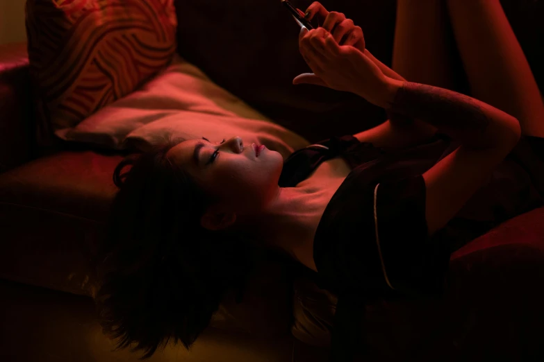 a woman laying on a couch holding a cell phone, inspired by Nan Goldin, happening, wong kar wai, 8 k sensual lighting, kiko mizuhara, of taiwanese girl with tattoos