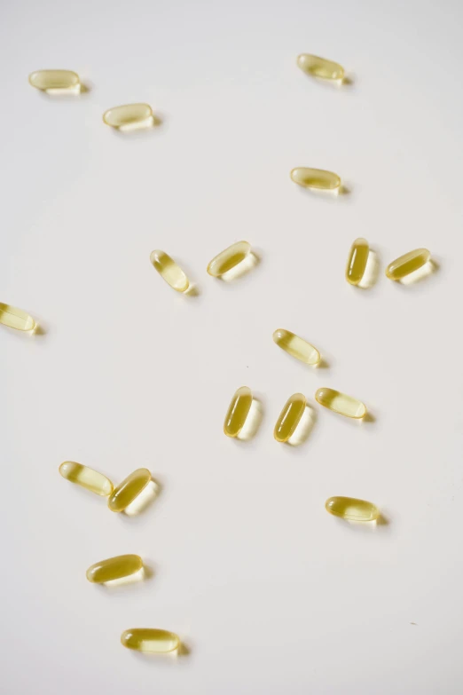 a pile of fish oil capsules on a white surface, by Jessie Algie, antipodeans, yellow hue, neuroscience, 12k, hemp