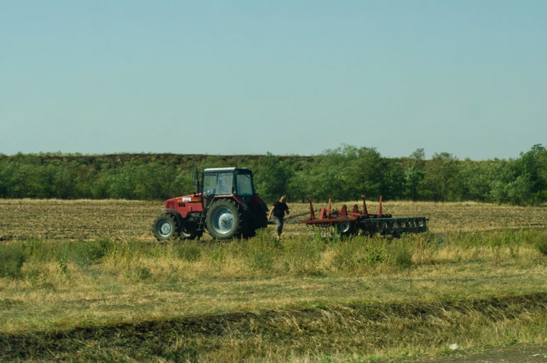 a tractor that is sitting in the grass, by Attila Meszlenyi, pexels contest winner, figuration libre, working out in the field, prairie in background, heavy line work, seen from a distance