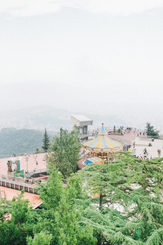 a group of people standing on top of a lush green hillside, a picture, inspired by Serafino De Tivoli, trending on unsplash, arabesque, amusement park buildings, damascus, foggy, carousel