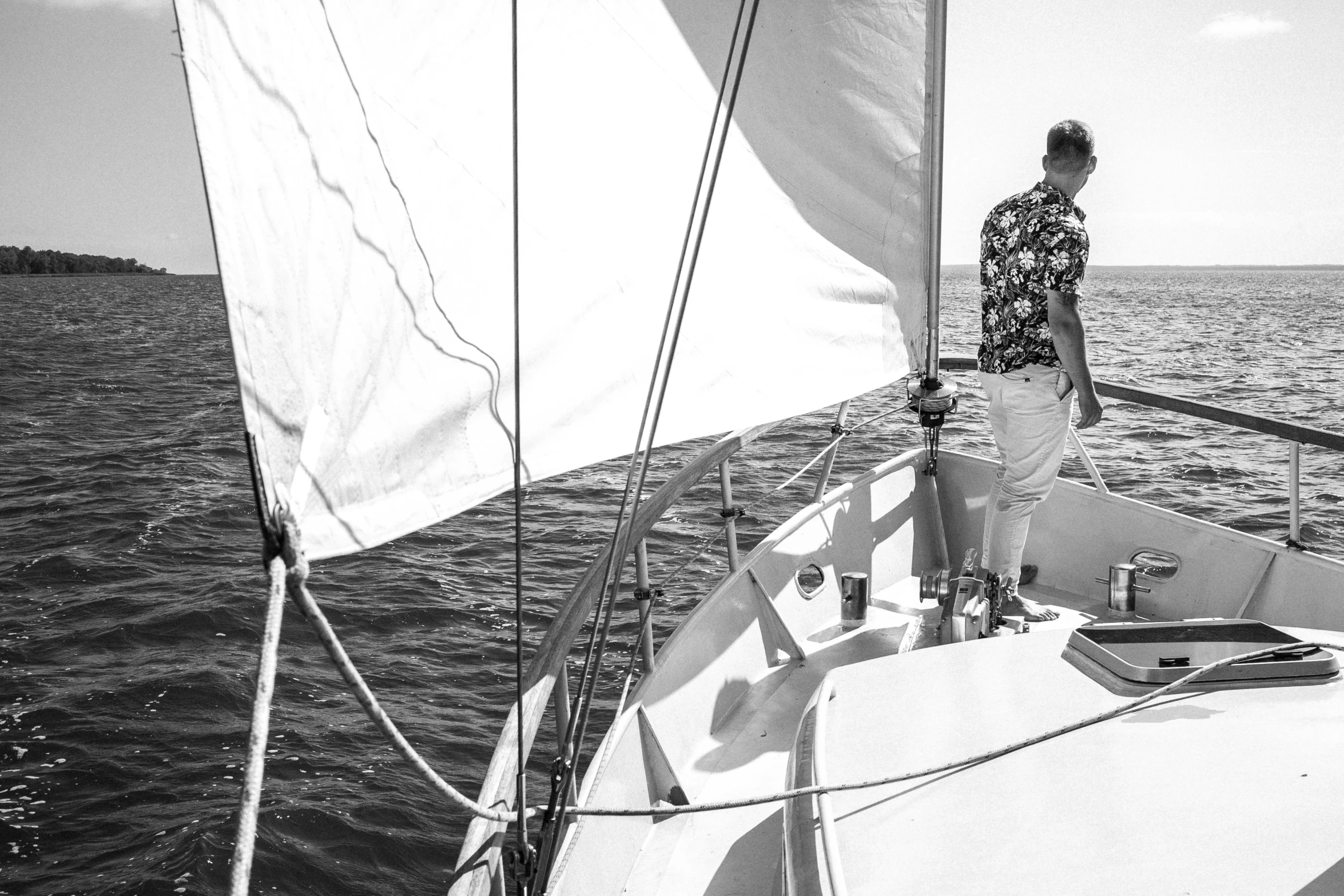 a man standing on the bow of a sailboat, a black and white photo, by Mathias Kollros, pexels contest winner, waring a hawaiian shirt, on a bright day, owen gent, by greg rutkowski