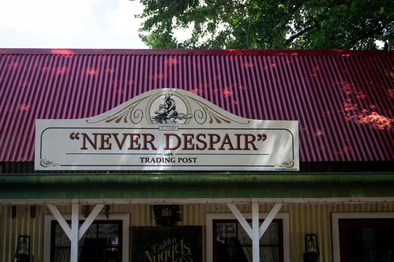 a building with a sign that says never despair, an album cover, inspired by Neil Blevins, trending on unsplash, art nouveau, taken in silver dollar city, outside a saloon, southern gothic scene, shop front