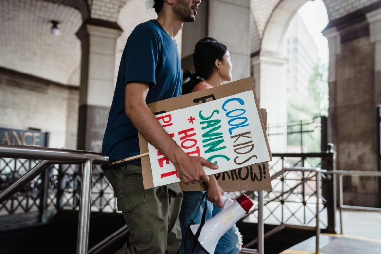 a man standing next to a woman holding a sign, by Julia Pishtar, pexels contest winner, nyc, cardboard, carrying a tray, schools