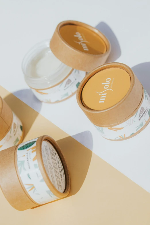 three jars of cream sitting on top of a yellow and white surface, a picture, by Olivia Peguero, unsplash, lyco art, packaging design, made of bamboo, wolfy nail, detailed product image