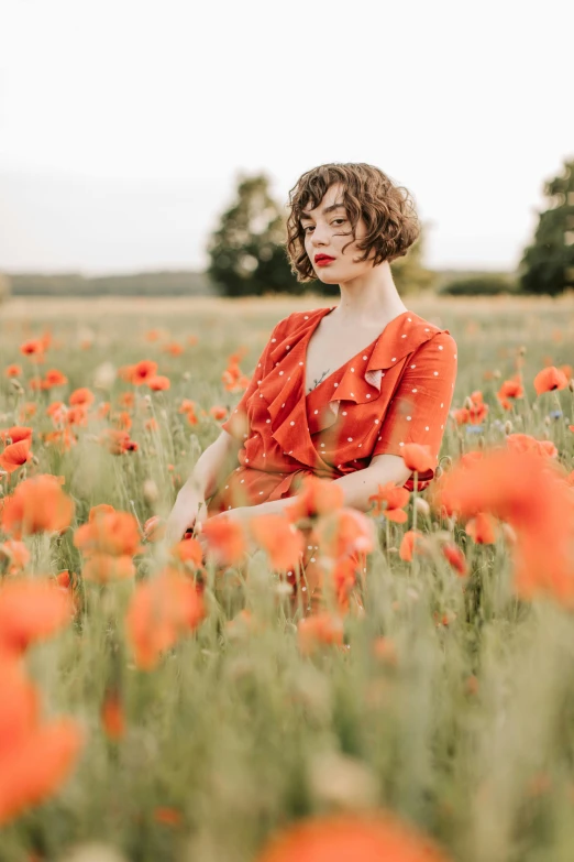 a woman sitting in a field of red flowers, wearing an orange jumpsuit, belle delphine, with short hair, european woman photograph