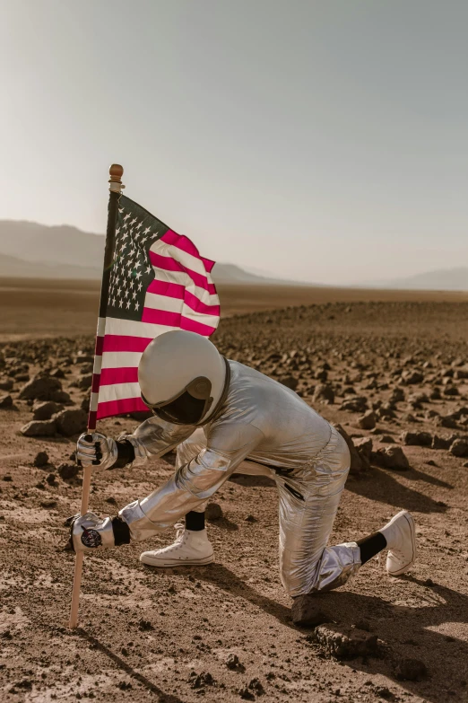 a man in a spacesuit holding an american flag, a colorized photo, unsplash contest winner, american romanticism, desert, inspect in inventory image, head down, ground broken