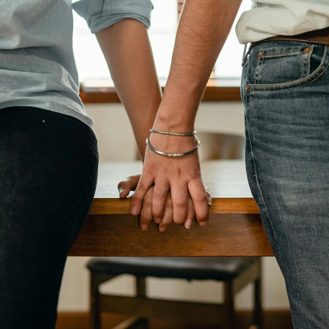 a close up of two people holding hands, a colorized photo, by Nina Hamnett, trending on reddit, standing on a desk, wearing steel collar, on kitchen table, sitting on bench