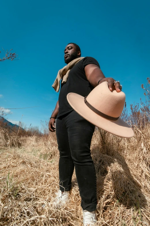 a man standing in a field with a hat, an album cover, pexels contest winner, man is with black skin, beefy, promotional still wide angle, thicc