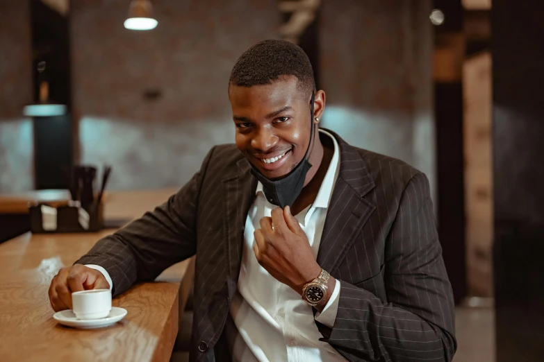 a man sitting at a table with a cup of coffee, smiling mask, mkbhd, wearing fashion suit, trending artstayion