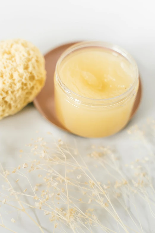 a jar of honey sitting on top of a wooden spoon, a picture, by Nicolette Macnamara, unsplash, sea sponges, bubble bath, panorama, beige