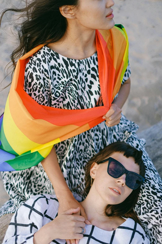 two women standing next to each other on a beach, by Julia Pishtar, pride flag in background, sunglasses and a scarf, flatlay, fabrics