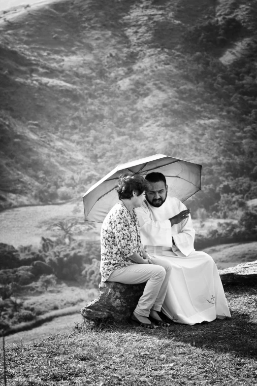 a man and a woman sitting under an umbrella, a black and white photo, by Max Dauthendey, baptism, on the mountain, loving, priest