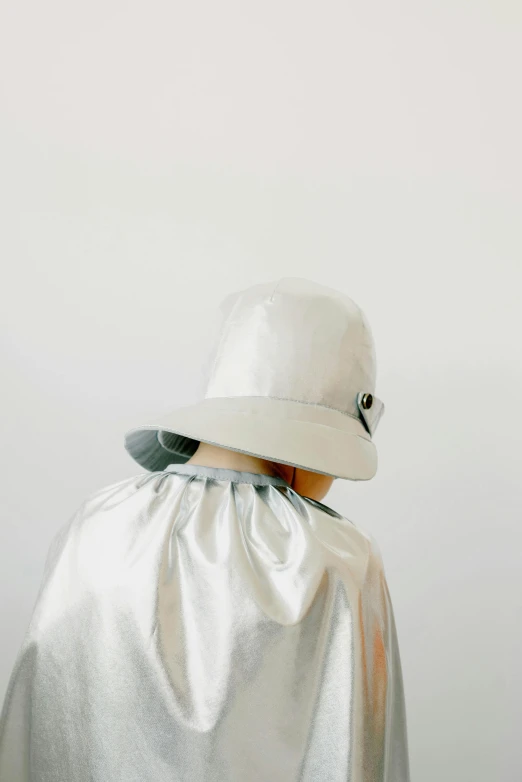 a person wearing a silver cape and a white hat, by Gawen Hamilton, unsplash, conceptual art, on a pale background, bucket hat, back - view, experimental studio light