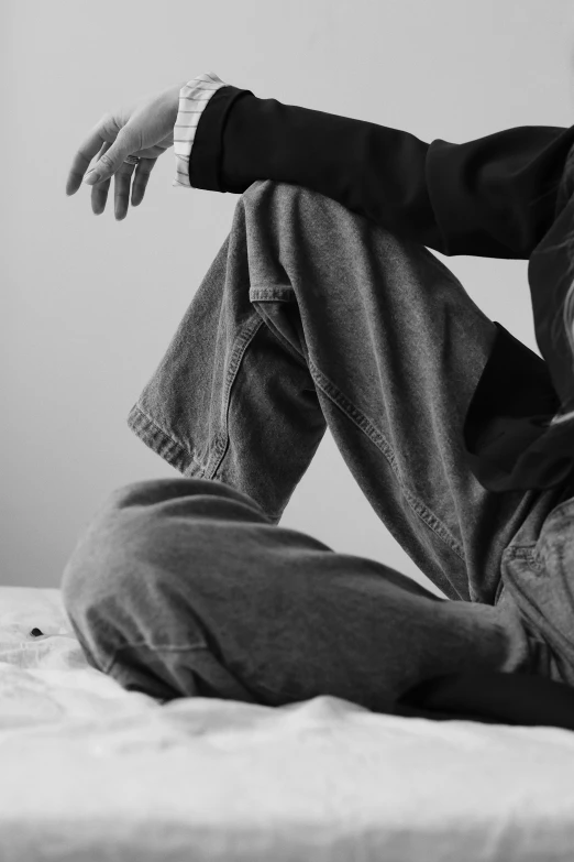 a black and white photo of a man sitting on a bed, unsplash, visual art, baggy jeans, large pants, closeup of arms, androgynous person