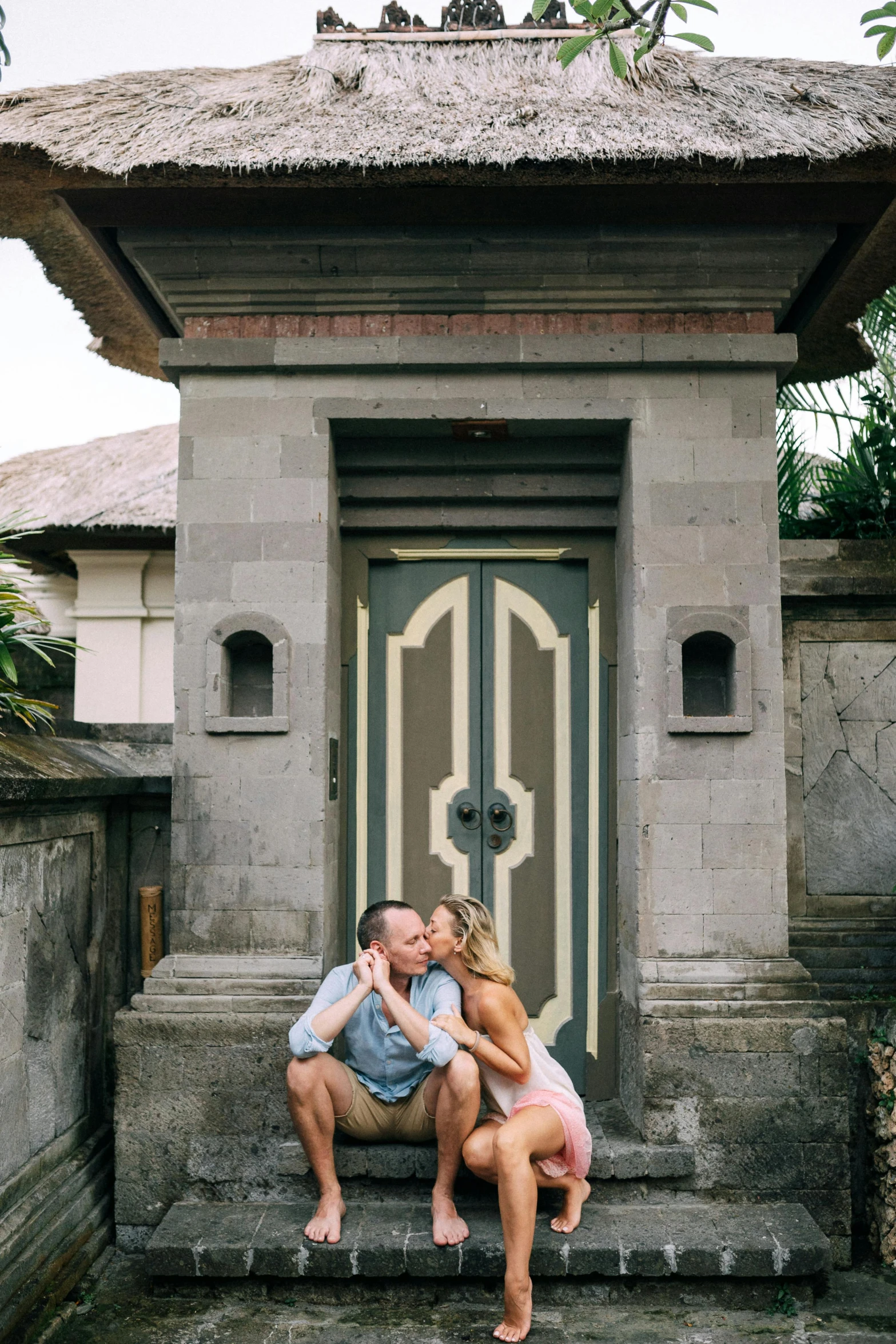 a man and a woman sitting on the steps of a building, bali, kissing together cutely, tall door, casey cooke