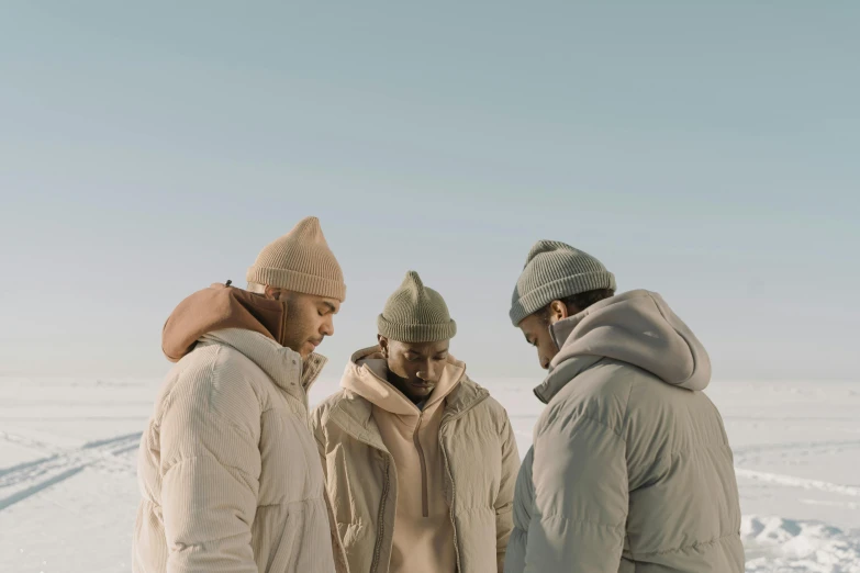 a group of people standing on top of a snow covered field, an album cover, trending on unsplash, symbolism, hat and hoodie, soft and muted colors, a portrait of issey miyake, three heads