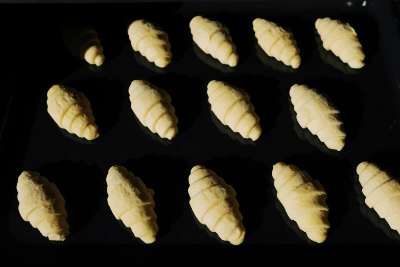 a tray of freshly baked croissants ready to go in the oven, inspired by Károly Patkó, surrealism, with a black background, 24mm, carved ivory, thumbnail