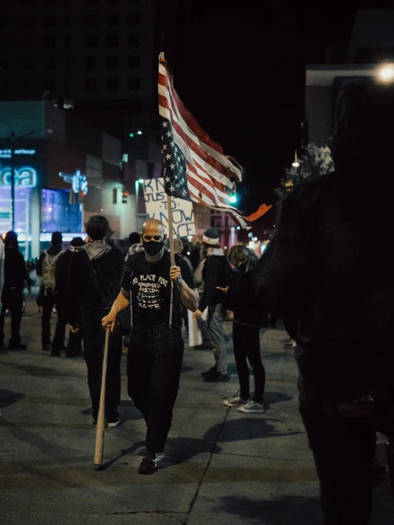 a group of people walking down a street at night, flag in his right hand, 2022 photograph, los angelos, ☁🌪🌙👩🏾