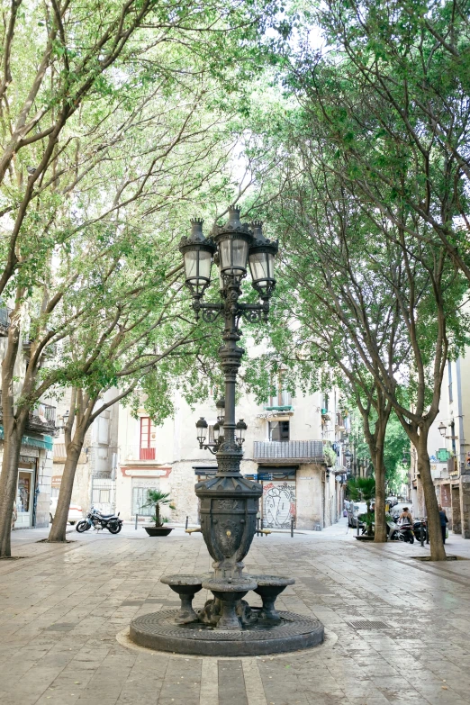 a lamp post sitting in the middle of a street, inspired by Tomàs Barceló, central tree, fountain, pristine and clean, shady alleys