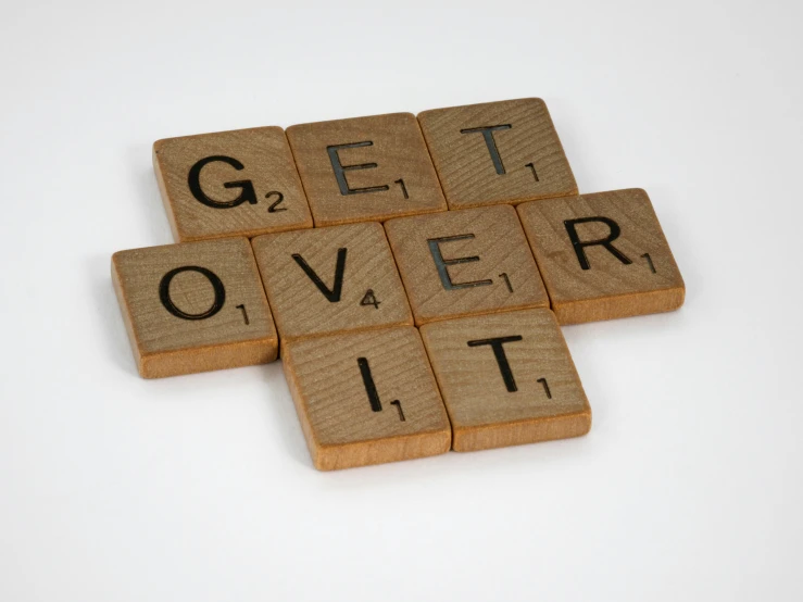 scrabbles spelling get over it on a white surface, a picture, by John Covert, excessivism, on wood, promotional image, beige, overdose