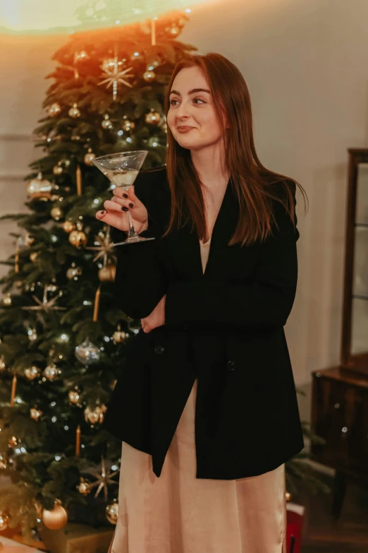 a woman standing in front of a christmas tree holding a wine glass, by Julia Pishtar, long black jacket, miranda otto, trending photo, elliot alderson