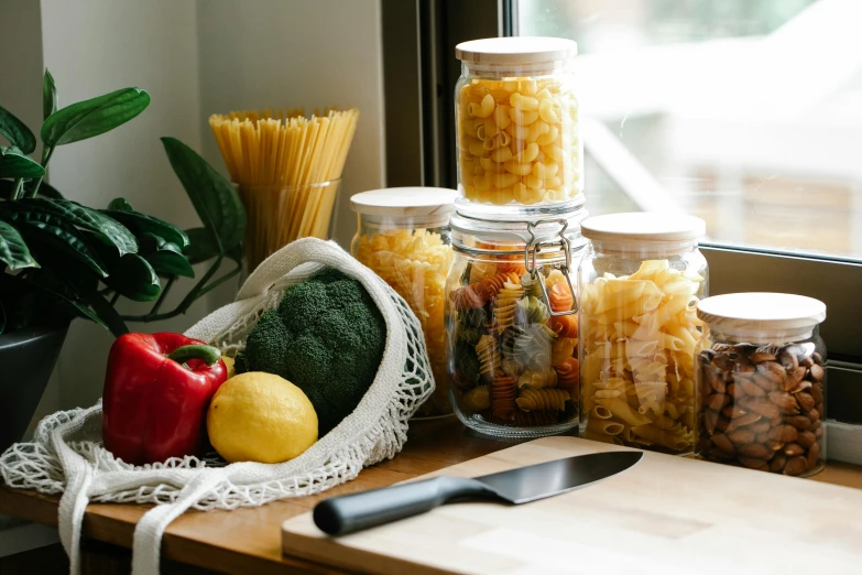 a table topped with lots of food next to a window, by Nicolette Macnamara, pexels contest winner, jar on a shelf, pasta, veggies, full product shot