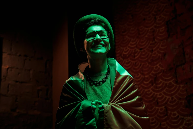 a man that is standing in the dark, she is smiling, dressed in a green robe, queer woman, set photograph in costume