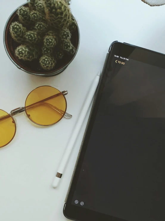 a tablet computer sitting on top of a white table, by Robbie Trevino, trending on unsplash, minimalism, yellow carrera glasses, next to a plant, round sunglasses, pencil