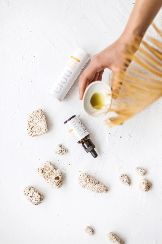 a close up of a person holding a bottle of essential oils, unsplash, in a white boho style studio, seeds, ochre, bulky build