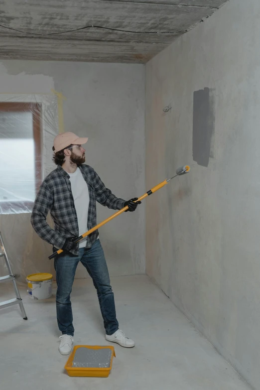 a man standing next to a ladder in a room, a hyperrealistic painting, pexels contest winner, using a spade, smooth solid concrete, thumbnail, wall ]