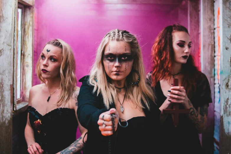 a group of women standing next to each other, an album cover, by Emma Andijewska, international gothic, wearing spikes and piercings, about to consume you, holding wands, evil vibe