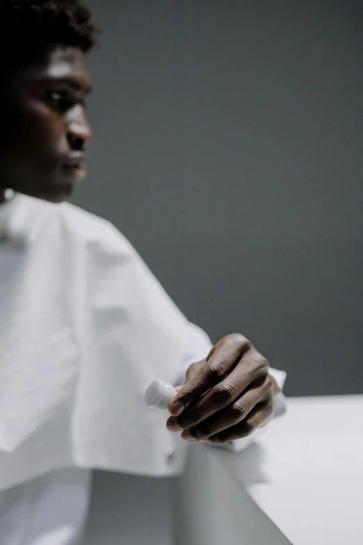 a close up of a person wearing a white shirt, inspired by Gordon Parks, unsplash, adut akech, surgical gown and scrubs on, holding hand, on a white table