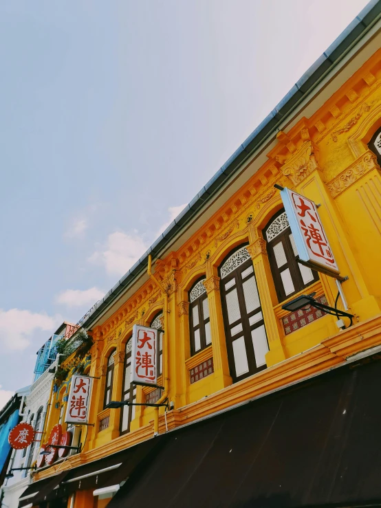 a tall yellow building sitting on the side of a street, pexels contest winner, set on singaporean aesthetic, intricate detailed roof, 🚿🗝📝, colorful signs